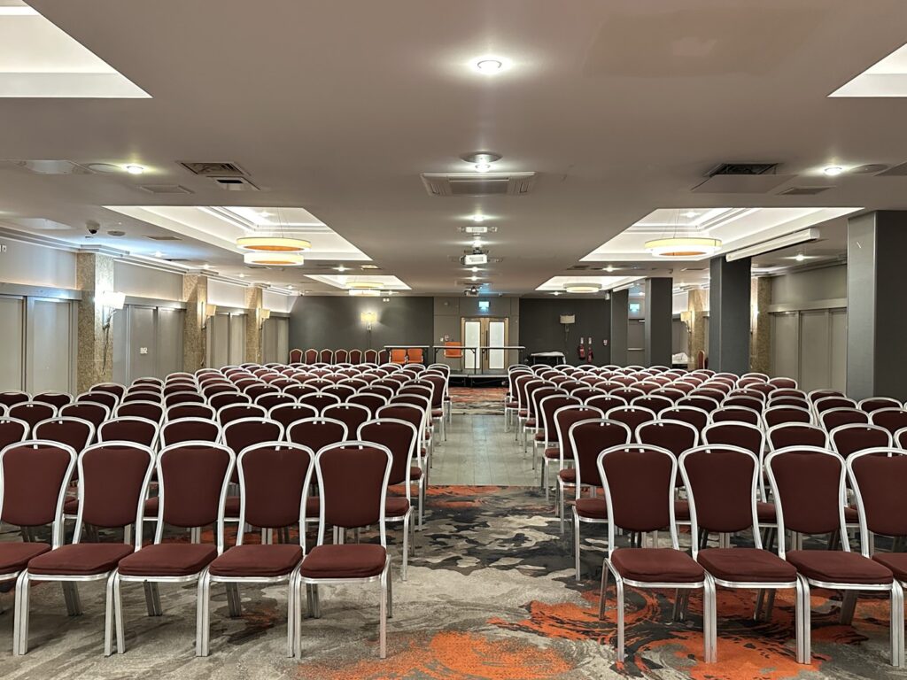 A conference in progress, theatre-style seating facing a stage at La Royale, Cricklewood